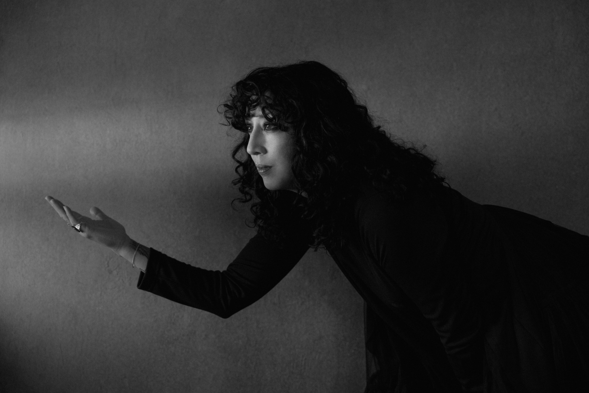 Clarice Jensen in black and white, reaching one hand forward in a shaft of light